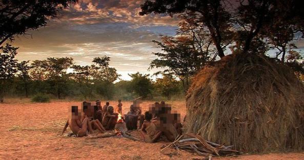 A group of people gathered around a fire at sunset, near a hut.