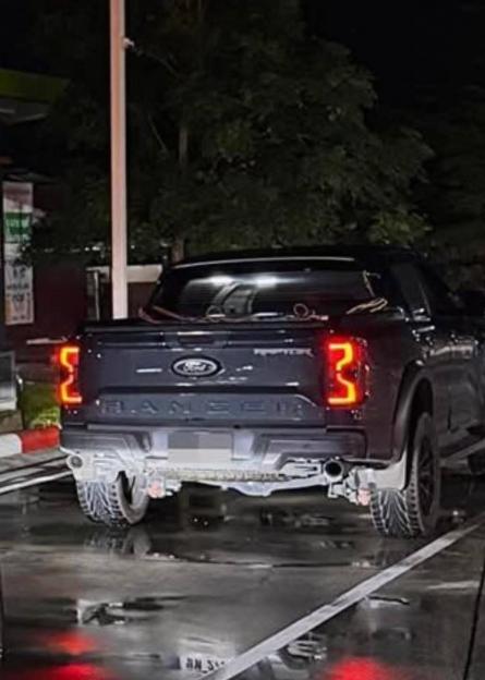 Rear view of a black Ford pickup truck at night with red taillights illuminated, on a wet road.