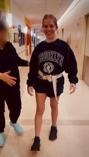 Woman in a hospital hallway relearning to walk with assistance.