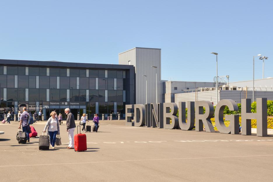 Exterior view of the Edinburgh Airport terminal and a large "EDINBURGH" sign.