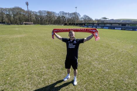 Pat Harding, son of former Chelsea manager Matthew Harding, holding a Hassocks Football Club scarf on the pitch.