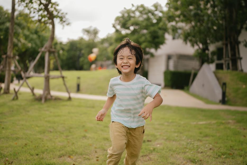 A boy with a joyful expression runs in a park.