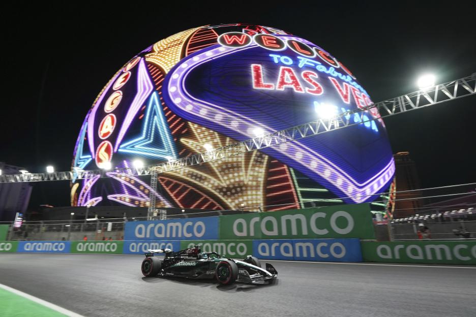 Mercedes driver George Russell in a black and green Formula 1 car on a warm-up lap with the illuminated "Welcome to Fabulous Las Vegas" sign in the background.