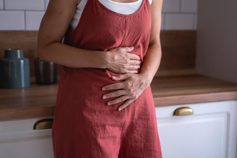 A woman in a red jumpsuit clutches her stomach, conveying discomfort.