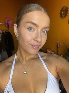 Woman wearing a white top and gold necklace.