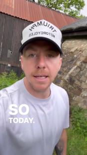 Man in a hat speaking in front of a stone wall.