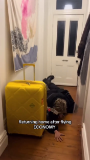 Person lying on the floor next to a yellow suitcase after flying economy.