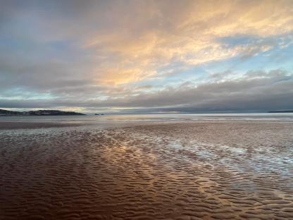 Sunset over a wet sandy beach.