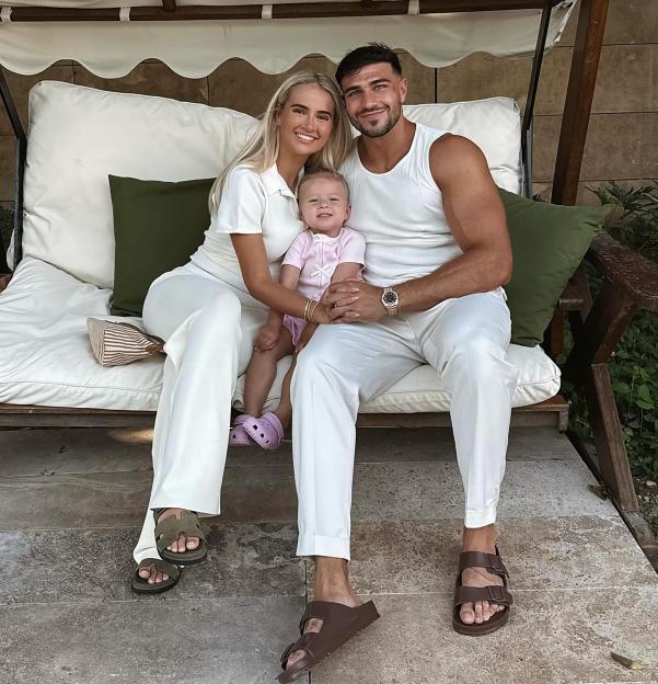 Tommy Fury, Molly Mae, and their baby daughter sitting together on a patio swing.