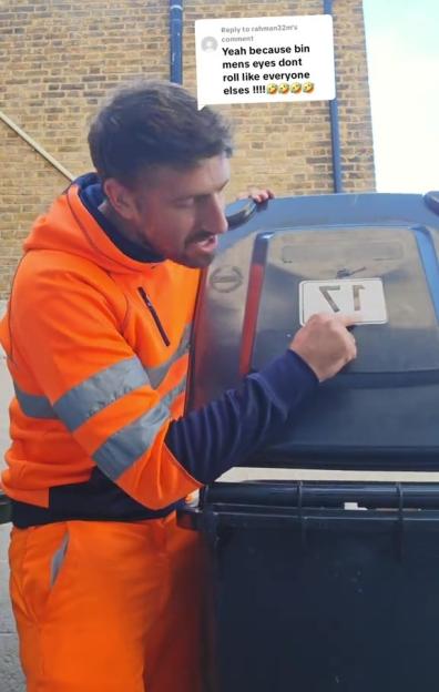 A binman in an orange uniform points to the inside of a black bin lid, where a label with a number is attached.