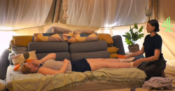 Screenshot of a woman lying on a couch while another woman attends to her feet.