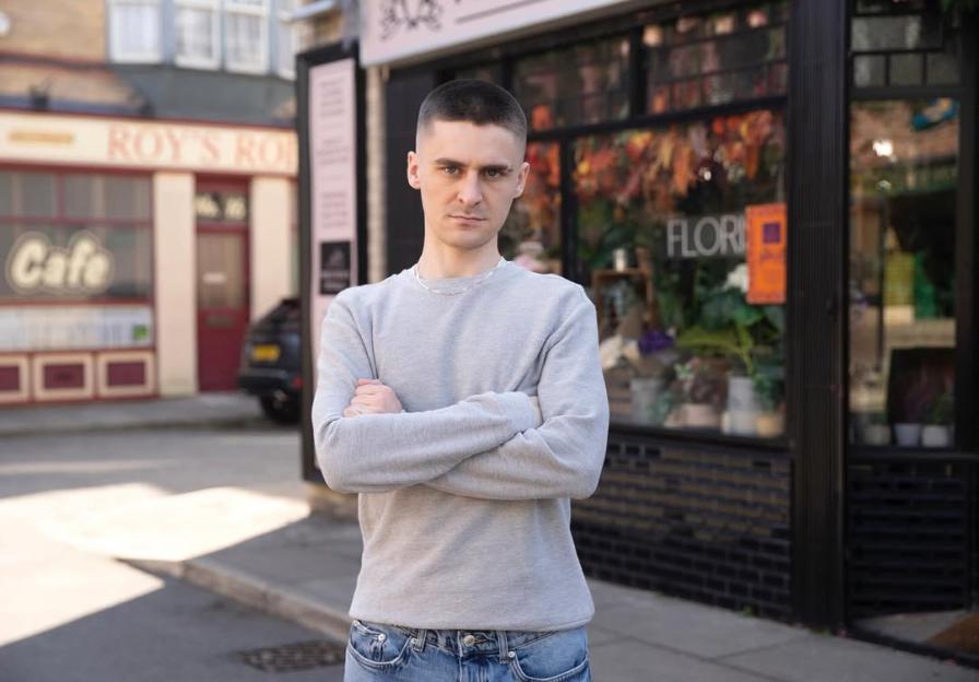 A man with arms crossed standing in front of a flower shop.
