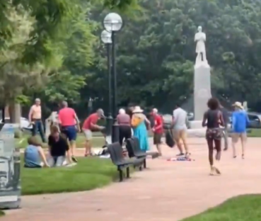 People gathering in a park near a statue.