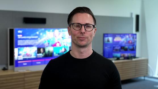 Man in glasses in front of televisions showing streaming content.