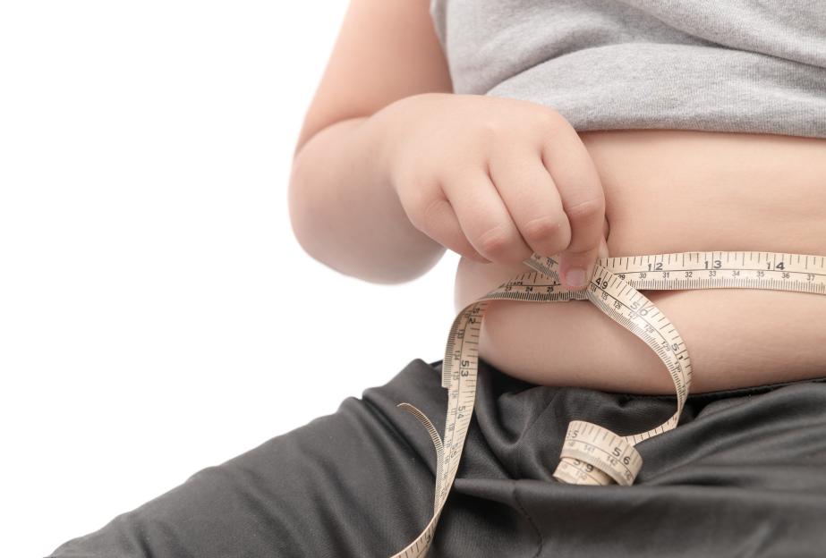Overweight child measuring waist with tape measure.