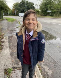 Boy in school uniform smiling outside school.