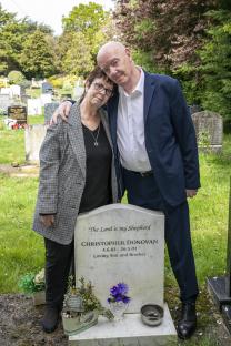 Couple standing by a gravestone in a cemetery.