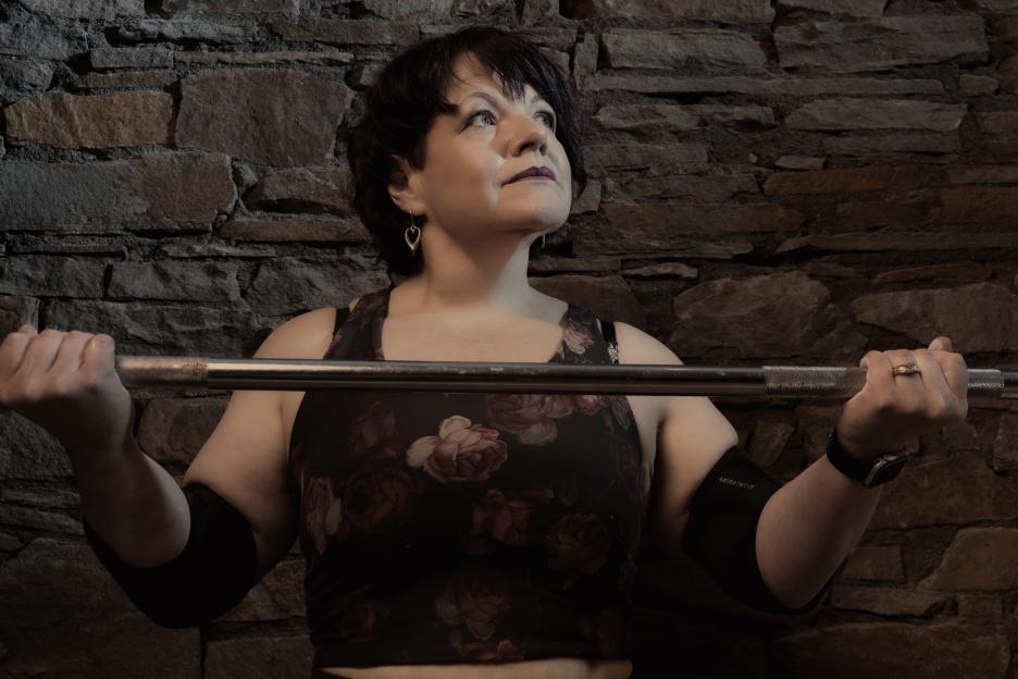 Woman weightlifting against a stone wall.
