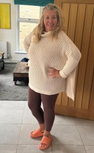 Woman in a cream sweater and maroon leggings standing in her home.