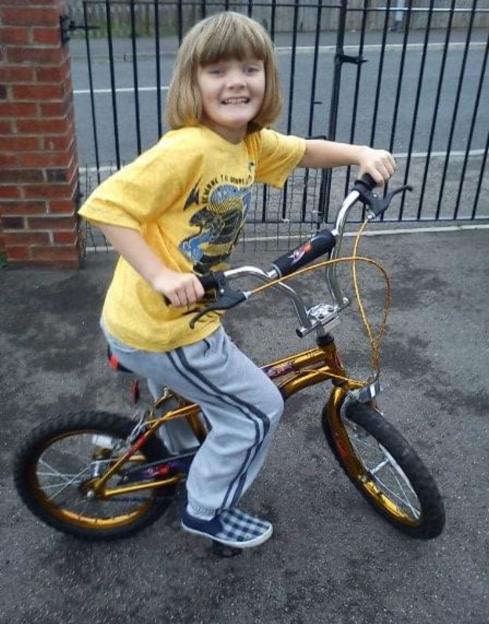 A young girl smiling while sitting on a gold bicycle.