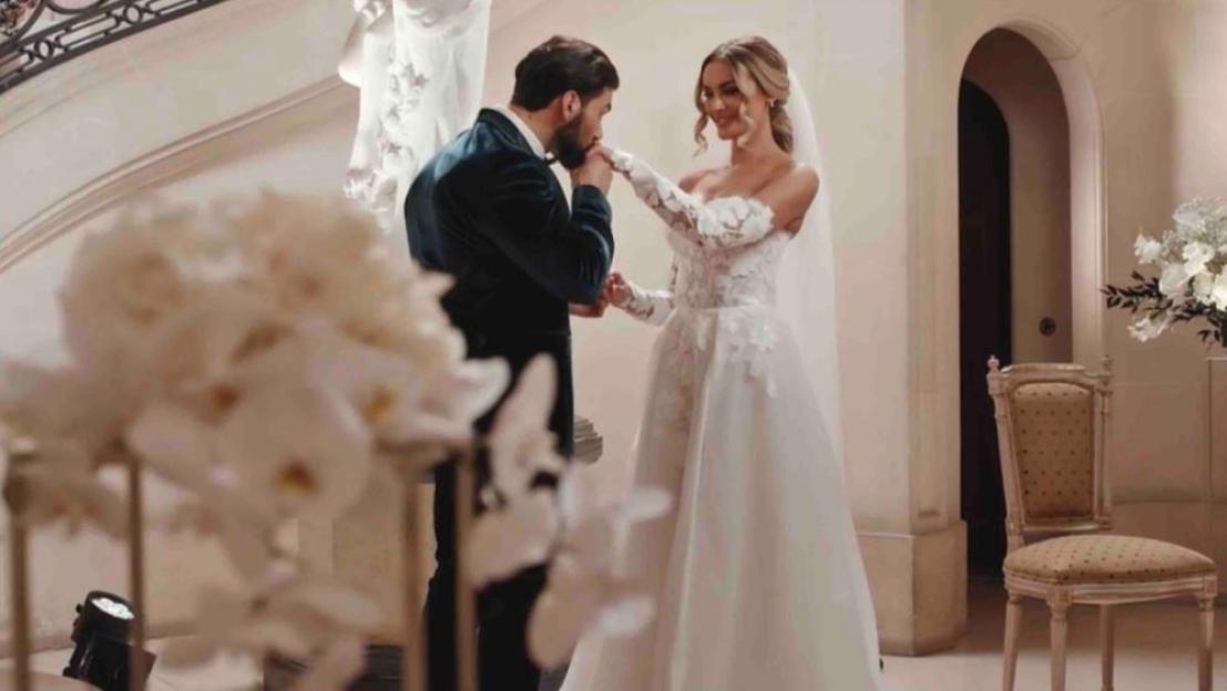 A man in a suit kisses the hand of a woman in a wedding dress.