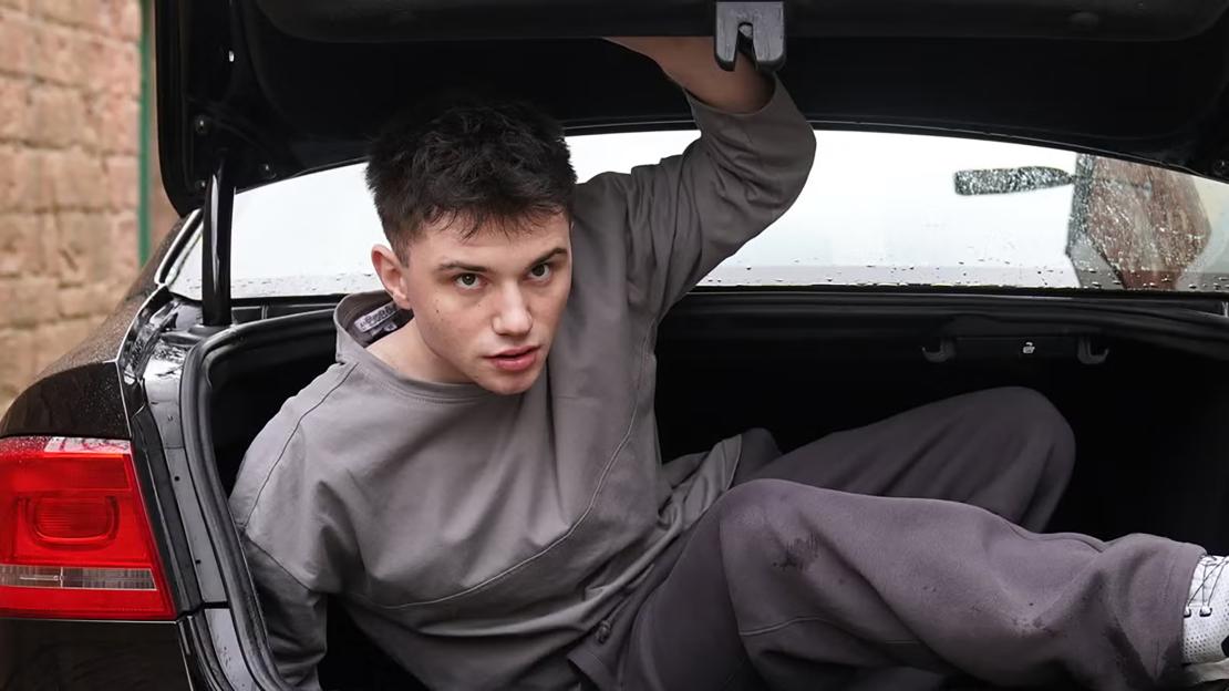 Zachary Sutcliffe as Bobby Costello in Hollyoaks, sitting in a car trunk.
