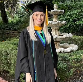 A woman in a graduation gown poses in front of a fountain.