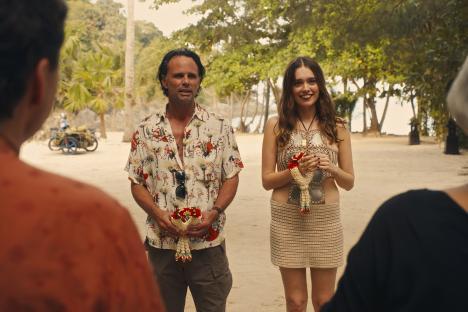 Two people holding flower leis on a beach.