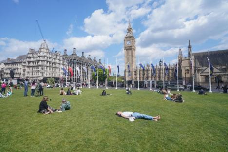 People relaxing on the grass in front of the Houses of Parliament and Big Ben.