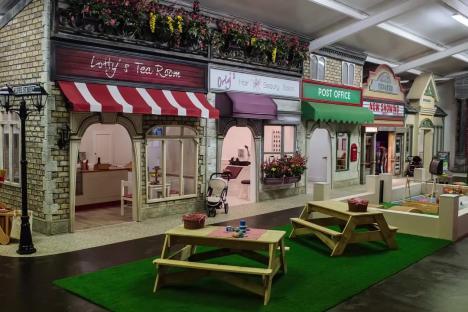 Indoor children's play village with shops and picnic tables.