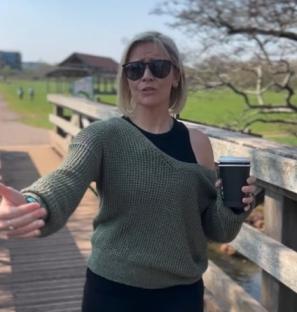 Woman in sunglasses holding a coffee cup on a bridge.