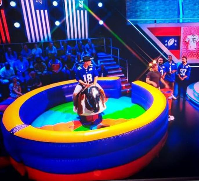 Dermot O'Leary riding a mechanical bull on a game show.