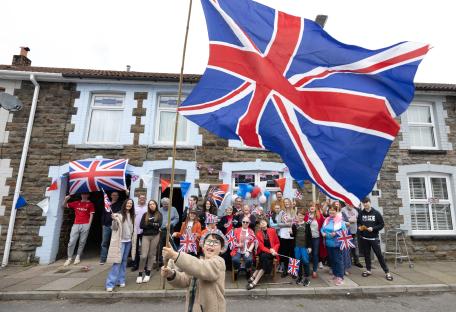 A boy waves a large Union Jack flag in front of a crowd of people celebrating the Coronation of King Charles III.