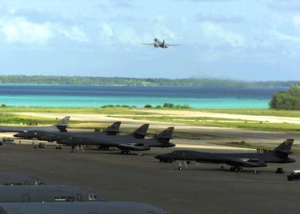 Photo of B-1 bombers on a runway with a B-1 taking off in the background, overlooking a tropical atoll.