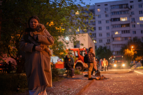 Woman holding a small dog in front of a building at night.