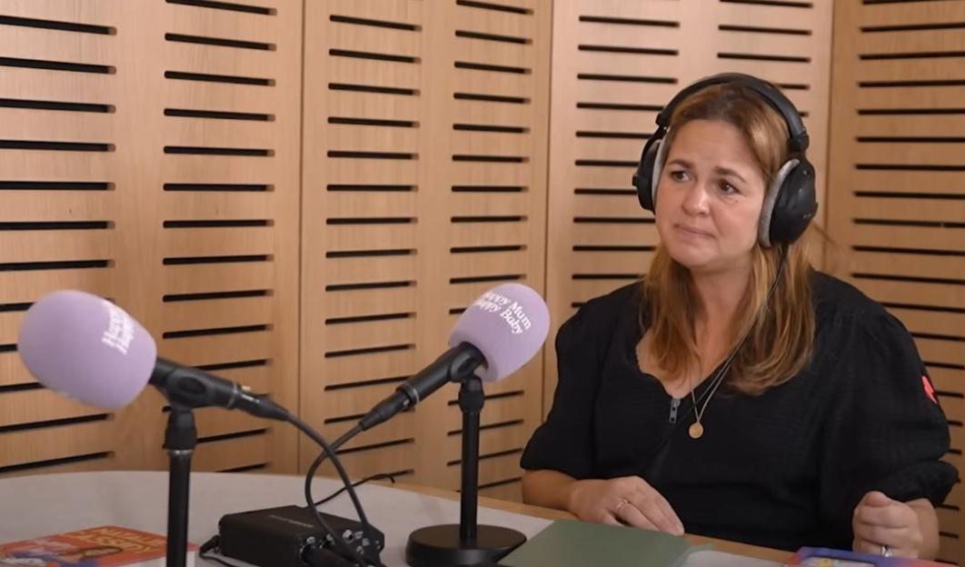 Natalie Cassidy wearing headphones and speaking into a microphone with "Happy Mum Happy Baby" on it.