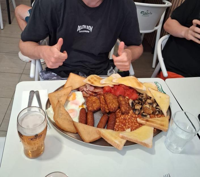 Man giving thumbs up with a large full English breakfast and beer.