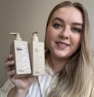 Person holding Arkive shampoo and conditioner bottles.
