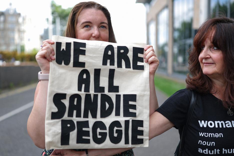 Woman holding a sign that says "We are all Sandie Peggie."