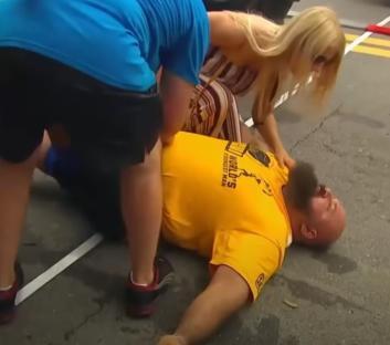 Strongman lying on the ground, being attended to by two people.