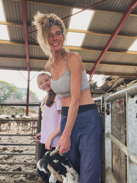 Amanda Owen with her daughter in a barn, holding a sheep.