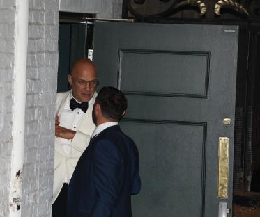 Two men in suits talking outside a dark green door.