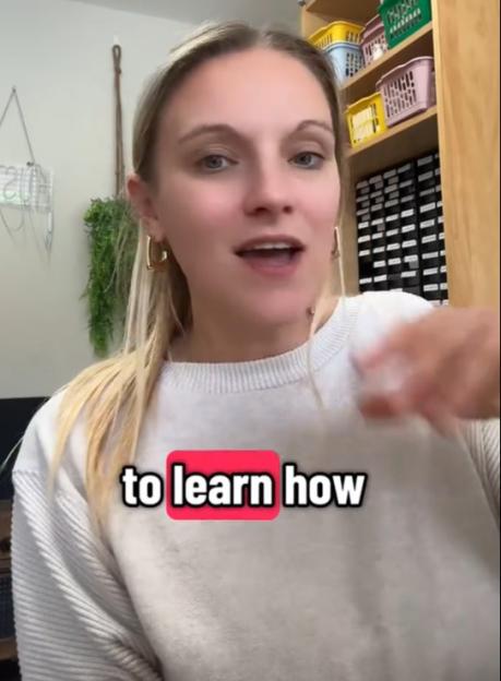 A blonde woman in a white sweater speaking to the camera with the text "to learn how" on her chest.