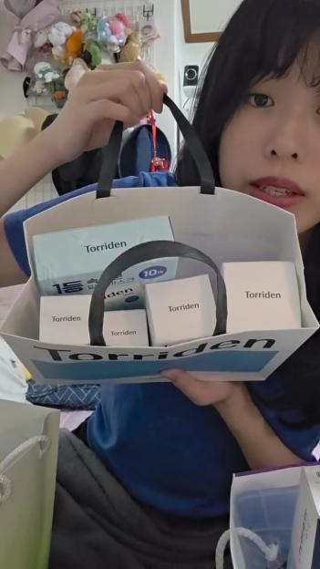 A young woman holding a shopping bag filled with several Torriden brand skincare products.