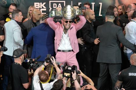 Conor McGregor holding up a championship belt at a weigh-in.