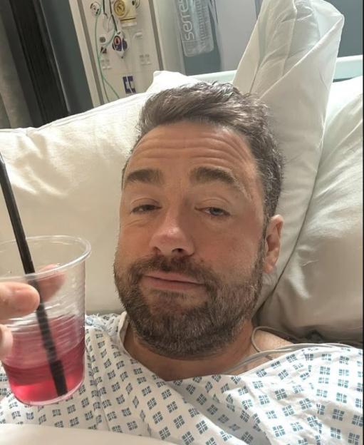 Man in hospital bed holding a drink.