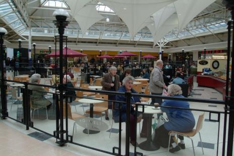 Interior of a shopping center's cafe area with people sitting at tables.