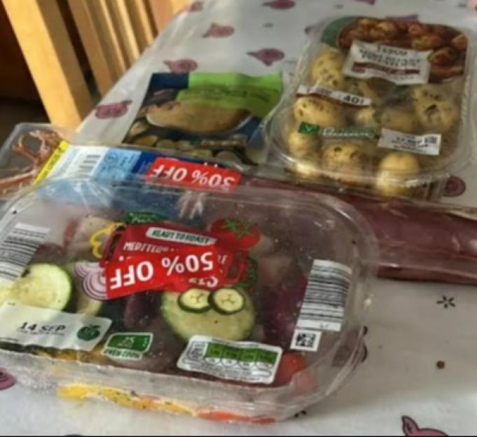 A package of ready-to-roast Mediterranean vegetables with a "50% OFF" sticker, next to packages of potatoes and other food items, on a table with a pig-patterned tablecloth.