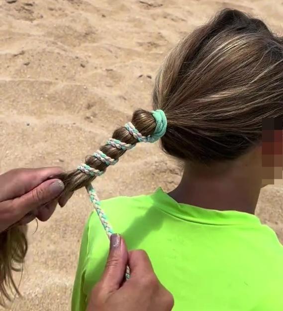 A child's hair being styled with rope to prevent tangling at the beach.