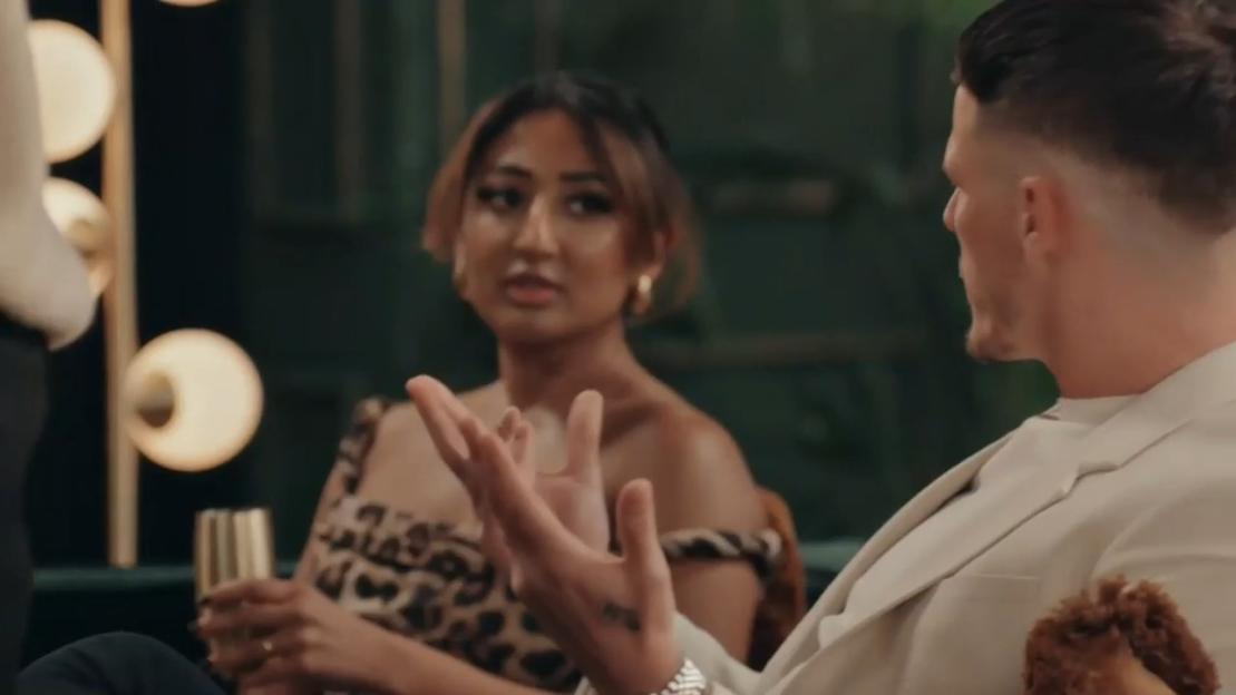 Man with short hair and a woman with an off-the-shoulder leopard print dress and gold hoop earrings having a tense conversation.
